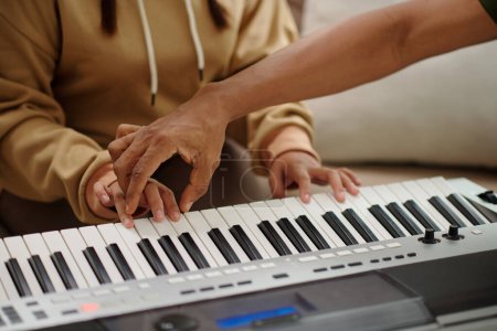 Photo for Teacher putting hand of student on synthesizer when explaining how to play chords - Royalty Free Image