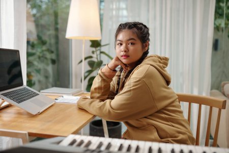 Téléchargez les photos : Portrait of teenage girl sitting at desk with opened laptop and looking at camera - en image libre de droit
