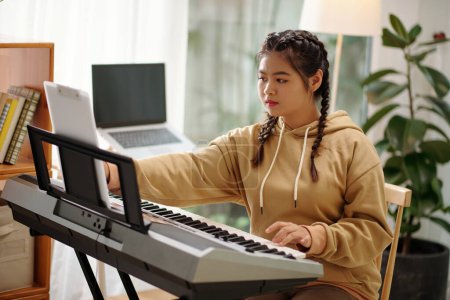 Foto de Talented teenge girl playing song on synthesizer at home - Imagen libre de derechos