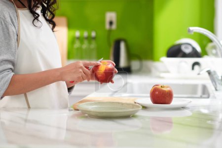 Téléchargez les photos : Mains de femme épluchant la pomme rouge lors de la fabrication de tarte pour le dessert - en image libre de droit
