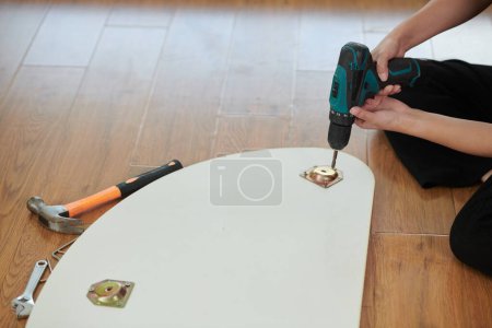 Woman drilling coffee table surface when assembling furniture