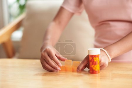 Téléchargez les photos : Woman putting pills in plastic container to take daily - en image libre de droit