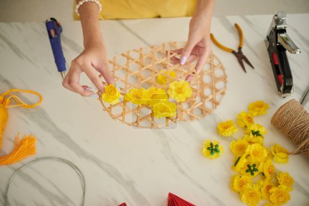 Foto de Woman glueing plastic apricot flowers on round base when making Tet decorations - Imagen libre de derechos