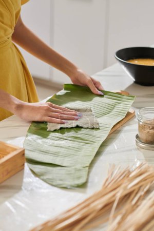 Photo for Woman wiping banana leaf for packing square cake - Royalty Free Image