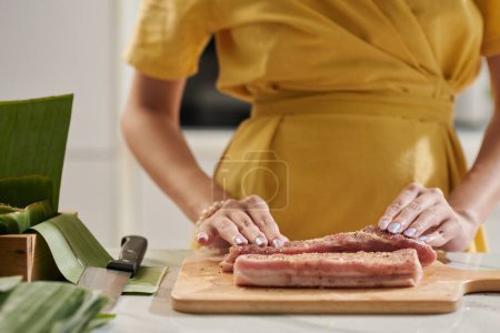 Téléchargez les photos : Femme assaisonnement morceaux de porc lors de la cuisson gâteau carré pour Tet - en image libre de droit