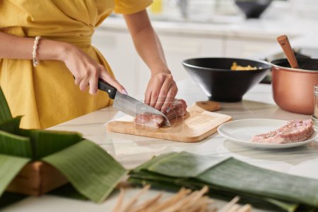 Photo for Closeup image of woman cutting seasoned pork in small pieces when cooking traditional cake for Tet - Royalty Free Image