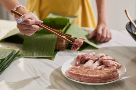 Téléchargez les photos : Woman adding pork pieces in mold covered with banana leaves - en image libre de droit