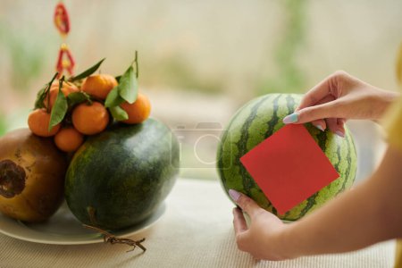 Photo for Hands sticking red note on ripe watermelon prepared for Tet celebration - Royalty Free Image