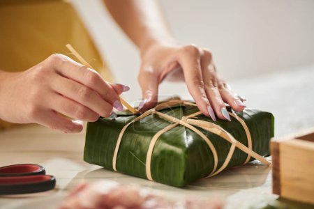 Photo for Hands of woman packing rice cake in banana leaves for spring festival - Royalty Free Image