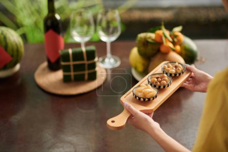 Téléchargez les photos : Femme apportant plateau de service avec oignons marinés et daikon à la table du dîner Tet - en image libre de droit