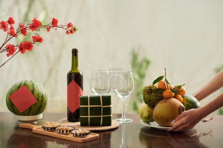Téléchargez les photos : Mains de femme mettant assiette avec des fruits frais sur la table servi pour le Nouvel An lunaire - en image libre de droit