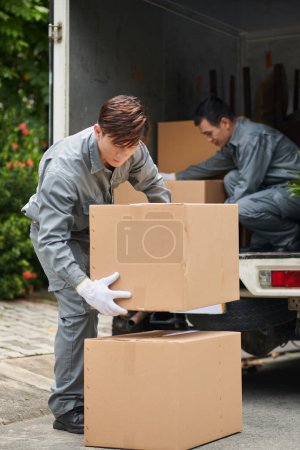 Foto de Movers unloading van with cardboard boxes, delivery service concept - Imagen libre de derechos