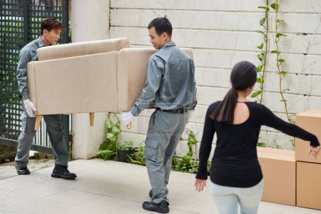Téléchargez les photos : House owner showing movers where to put new sofa she bought - en image libre de droit
