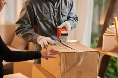 Téléchargez les photos : House owner controlling mover sealing cardboard boxes - en image libre de droit