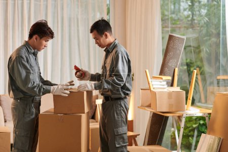 Photo for Team of movers packing personal items of client in cardboard boxes - Royalty Free Image