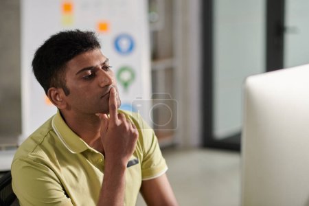 Foto de Portrait of pensive UX designer looking at computer screen deciding what to change in mockup - Imagen libre de derechos