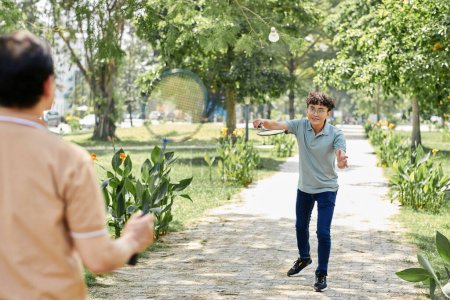 Photo for Smiling man playing badminton with his senior father in sunny park - Royalty Free Image