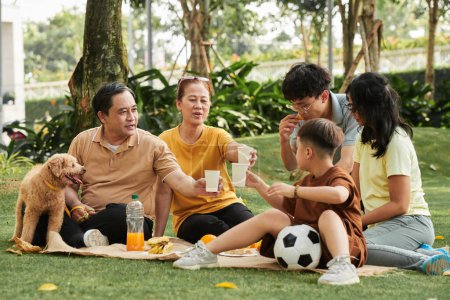 Photo for Family toasting with paper cups of juice when having picnic in park - Royalty Free Image