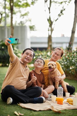 Photo for Smiling senior man taking selfie with his wife, grandson and dog - Royalty Free Image