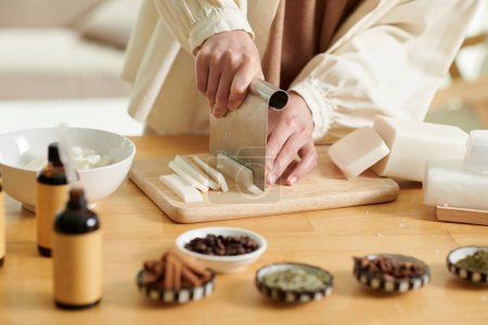 Téléchargez les photos : Closeup image of woman cutting soap base in thin slices when making cosmetics at home - en image libre de droit