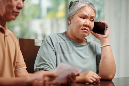 Téléchargez les photos : Sad senior woman receiving phone call from bank after missing credit card payment - en image libre de droit