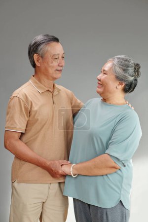 Photo for Senior couple in love standing against grey background and looking at each other - Royalty Free Image