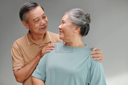 Photo for Cheerful senior husband and wife looking at each other when standing against grey background - Royalty Free Image