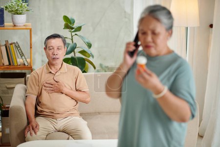 Photo for Senior man suffering from sudden heartache when his wife calling doctor to ask which medicine to take - Royalty Free Image