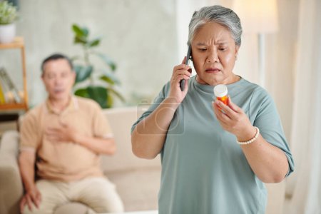 Téléchargez les photos : Femme âgée inquiète appelant le médecin pour demander si elle peut donner des pilules au mari souffrant de chagrin d'amour - en image libre de droit