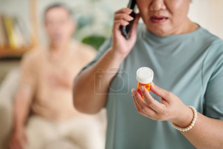 Téléchargez les photos : Aged woman calling doctor to ask about medical contraindications before giving pills to husband - en image libre de droit