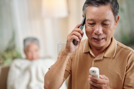 Senior man calling doctor after measuring body temperature of his wife with electronic thermometer