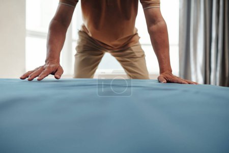 Cropped image of senior man changing sheets in bedroom
