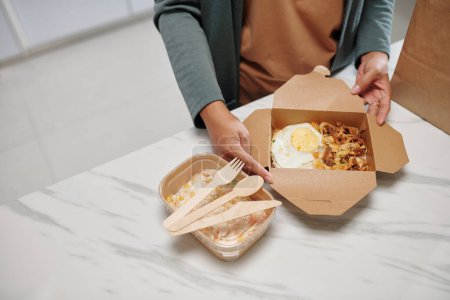 Hands of housewife opening box with delicious food delivered from local restaurant