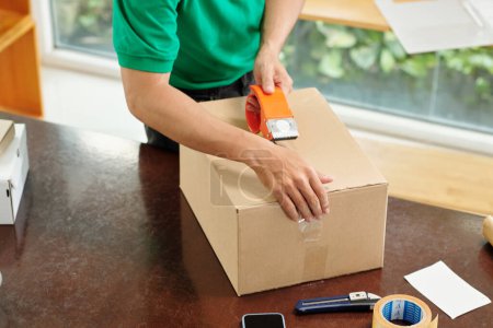 Téléchargez les photos : Hands of post worker sealing cardboard box for security - en image libre de droit
