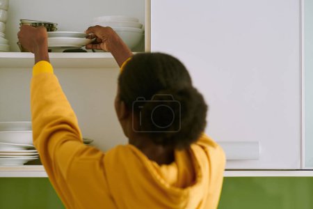 Téléchargez les photos : Femme mettant des assiettes propres dans l'armoire de cuisine - en image libre de droit