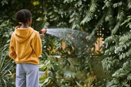 Photo for Young woman in comfy clothes watering trees in backyard in the morning - Royalty Free Image