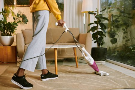 Téléchargez les photos : Cropped image of young woman vacuum cleaning floor in apartment - en image libre de droit