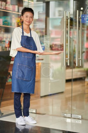 Téléchargez les photos : Travailleur souriant de l'épicerie invitant les clients à l'intérieur - en image libre de droit
