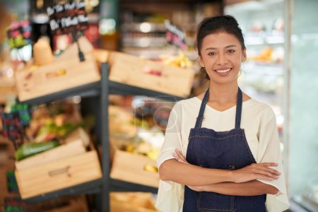 Téléchargez les photos : Portrait d'une travailleuse d'épicerie souriante debout les bras croisés - en image libre de droit