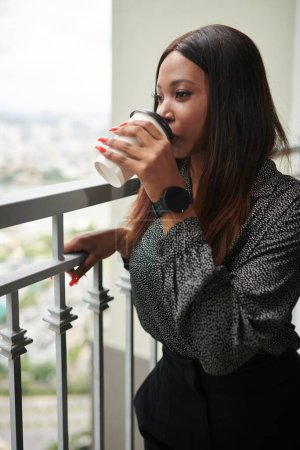 Photo for Portrait of young Black businesswoman standing on balcony, drinking coffee and enjoying the view - Royalty Free Image