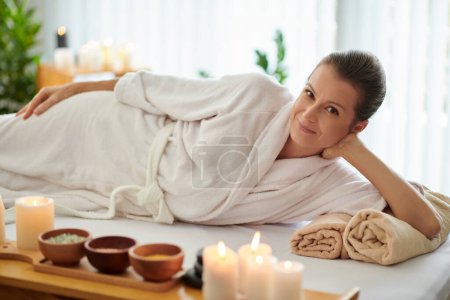 Foto de Mujer sonriente en albornoz relajándose en la cama en el salón de spa después de recibir masajes - Imagen libre de derechos