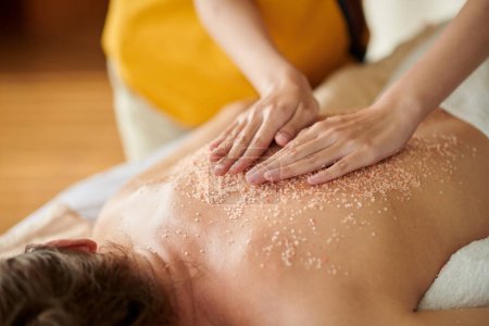 Photo for Masseuse massaging back of woman with salt scrub to get rid of dead skin cells - Royalty Free Image