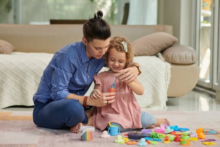 Foto de Madre explicando sonriente hija cómo hacer burbujas de jabón cuando están jugando en casa - Imagen libre de derechos