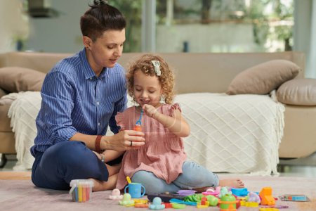 Foto de Madre pasar tiempo con su hija pequeña, que están jugando con juguetes y burbujas de jabón soplado - Imagen libre de derechos