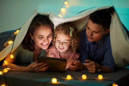 Téléchargez les photos : Happy family watching animated film on tablet computer when lying under blanket - en image libre de droit