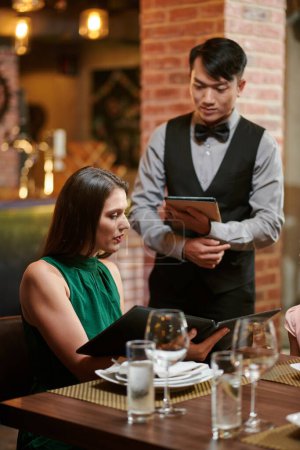 Téléchargez les photos : Young elegant woman telling waiter what she wants to order for dinner - en image libre de droit