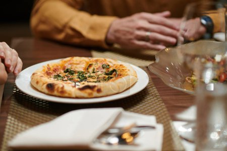Foto de Small pizza on plate in front woman eating dinner in restaurant - Imagen libre de derechos