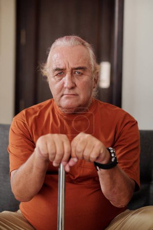 Téléchargez les photos : Portrait of frowning senior man leaning on walking stick and looking at camera - en image libre de droit