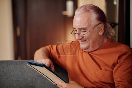 Téléchargez les photos : Homme âgé souriant lisant un livre électronique sur une tablette numérique - en image libre de droit