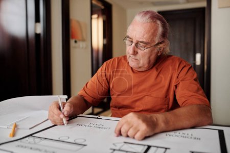 Téléchargez les photos : Senior homme dessin plan de construction pour sa maison lors de la planification de la rénovation - en image libre de droit